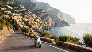 Route panoramique de la côte amalfitaine avec un scooter avançant paisiblement entre les falaises, les villages colorés et la mer Méditerranée.