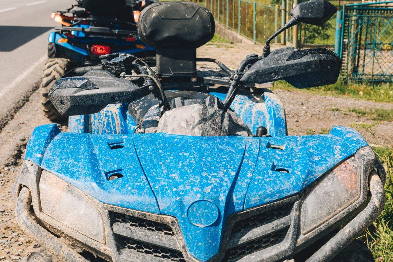 Un quad tracte un tondo-broyeur sur une prairie.